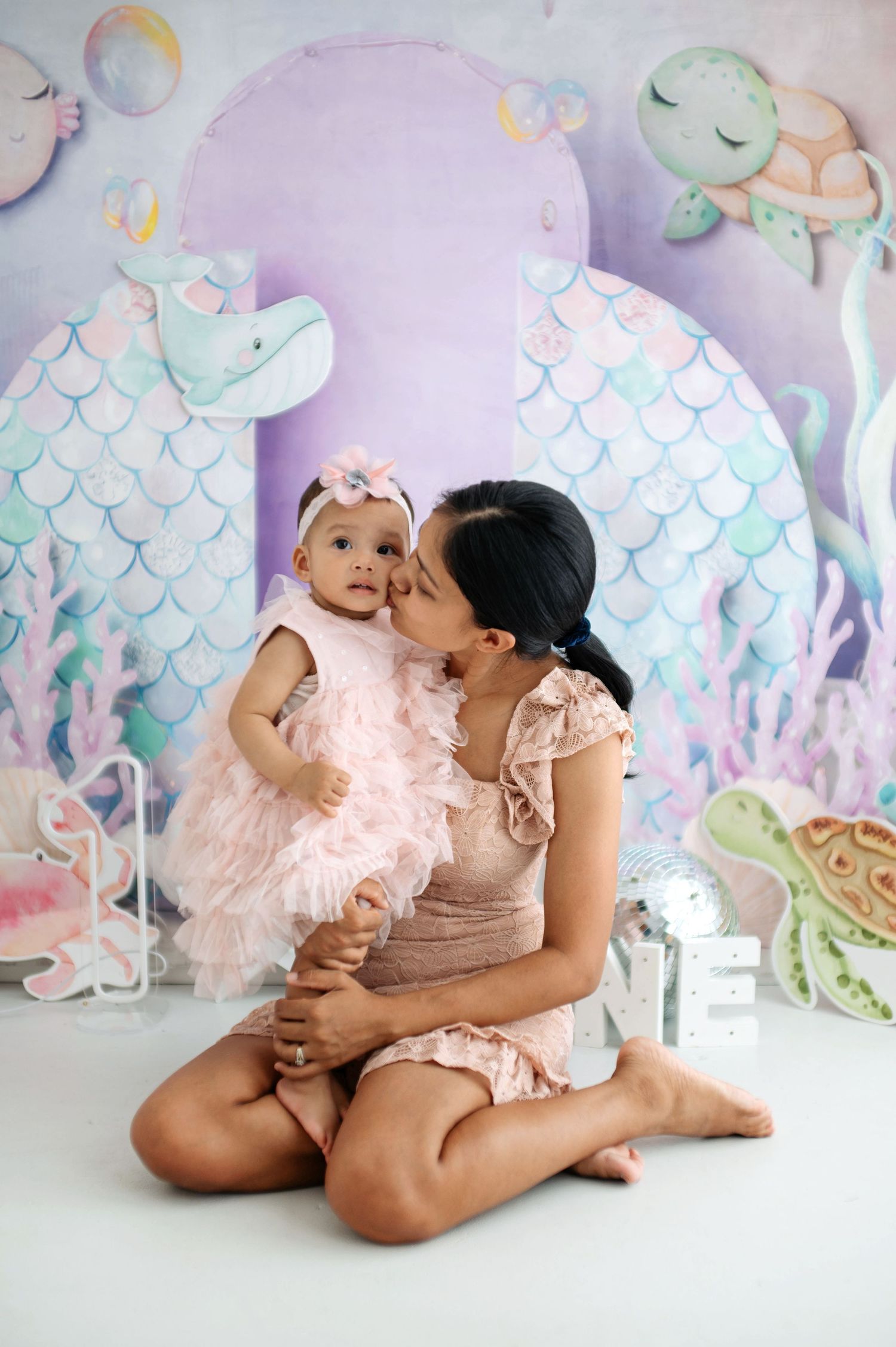 Parent and child share tender moment against dreamy mermaid-themed backdrop with pastel colors.