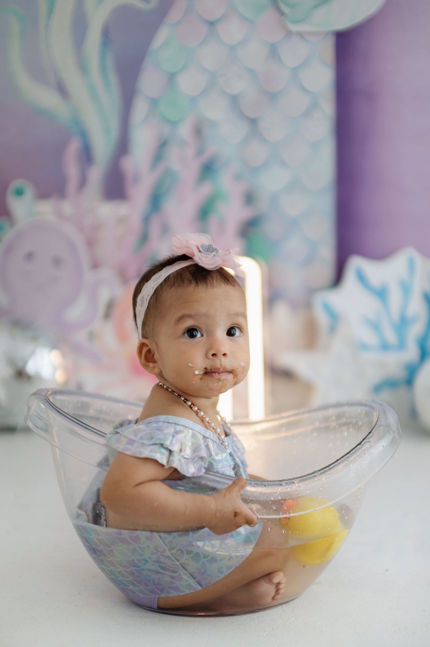 Baby in blue outfit enjoys cake smash photo session with clear bowl and yellow frosting.