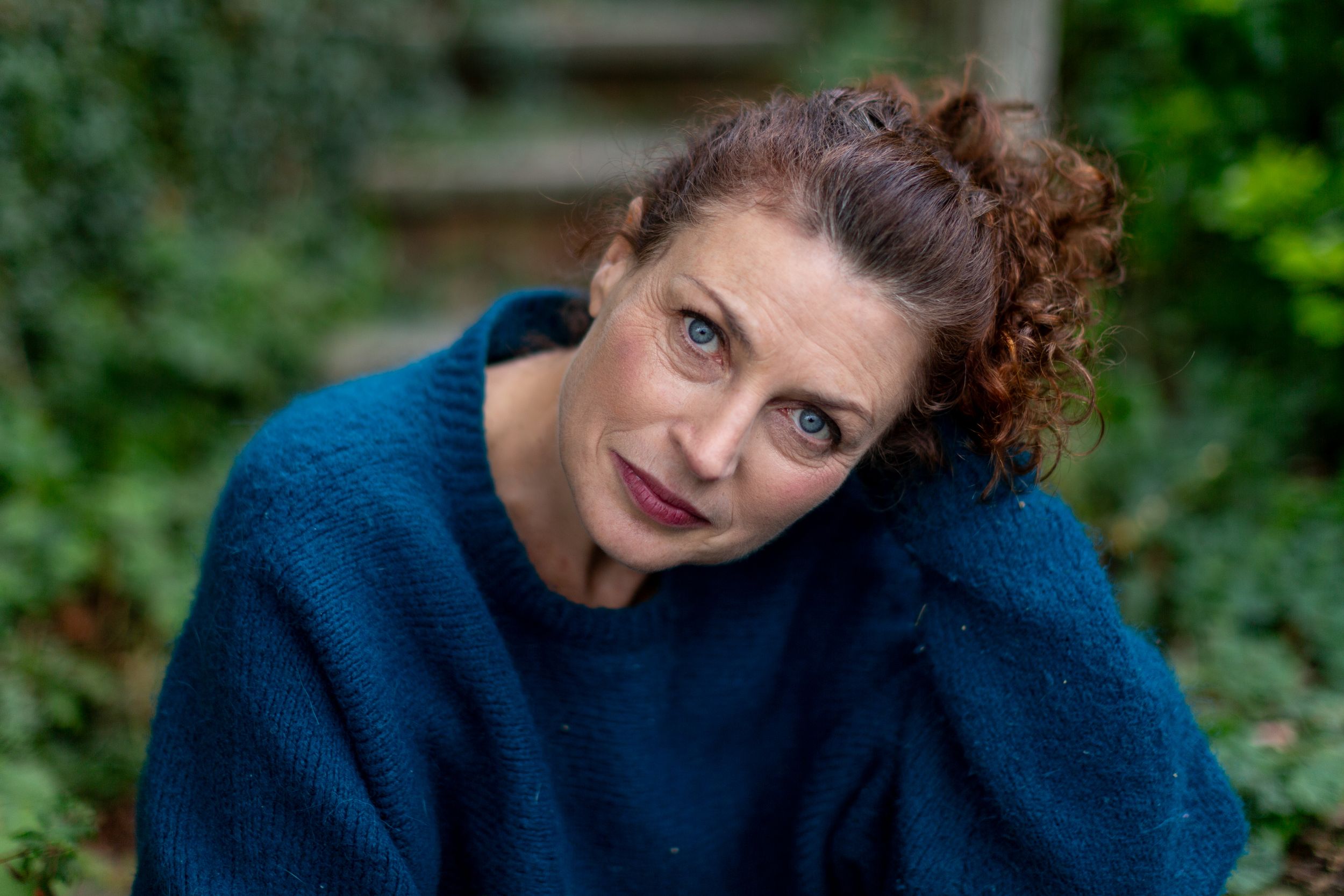 Woman with curly hair in navy blue sweater poses against green foliage background in a series of photos.