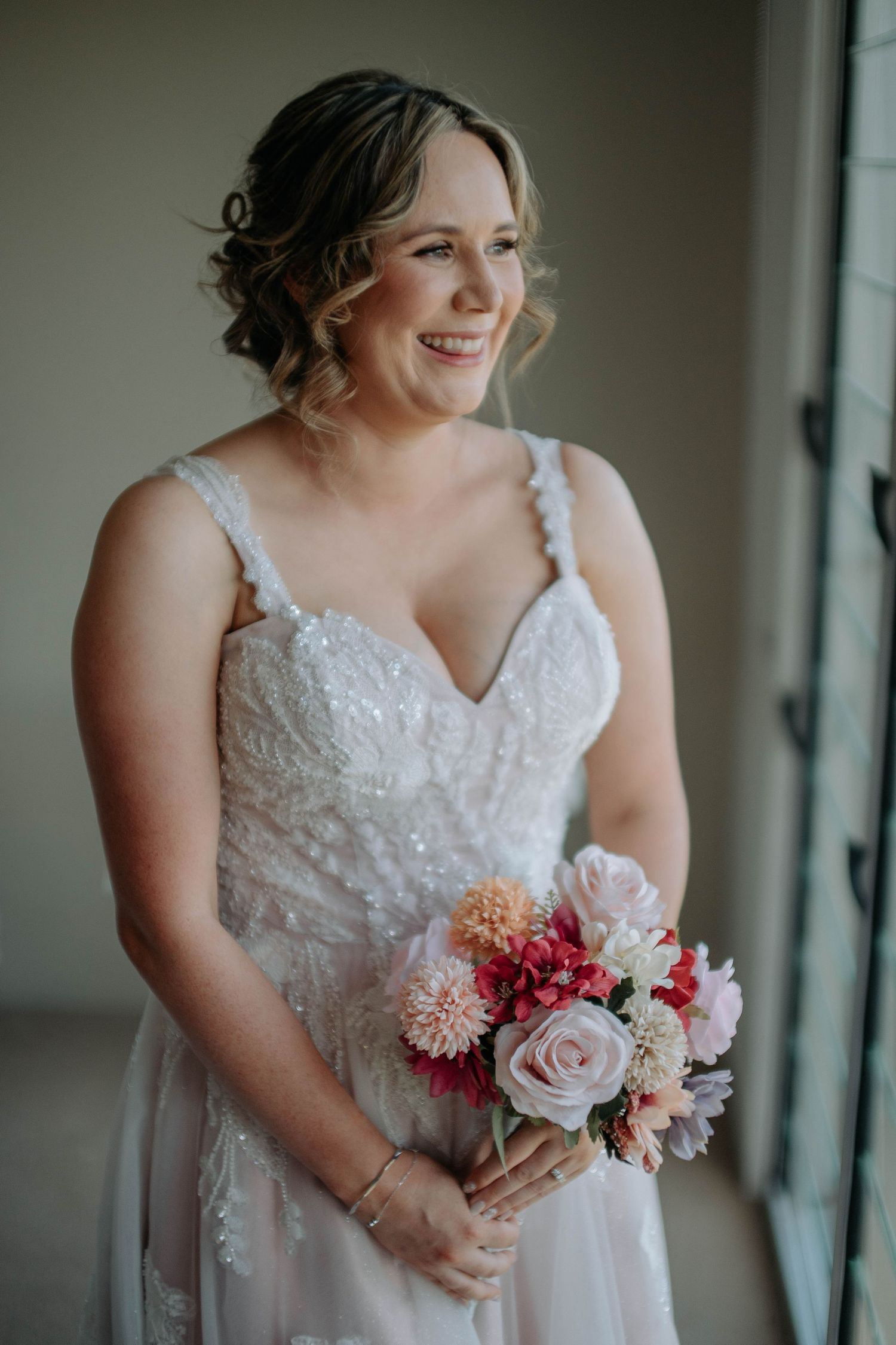 Close-up details of a white lace wedding dress with delicate beading and a pink and coral floral bouquet.