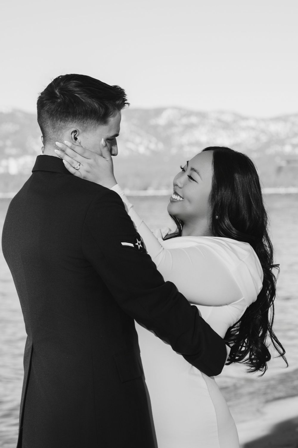 A romantic black and white photo series of a couple embracing by the water during a wedding photoshoot.