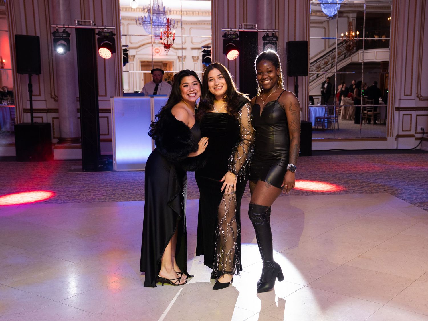 Dancers practicing in an elegant ballroom with chandeliers and pink ambient lighting.