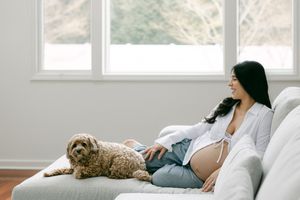 A pregnant woman relaxes on a white couch with a cat curled up beside her.