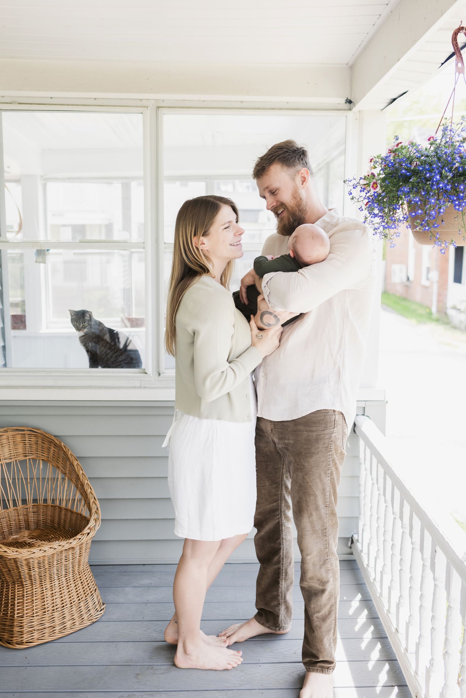 Proud parents hold their newborn baby boy wearing forest green on a famers porch in South Berwick, Maine for newborn photos.
