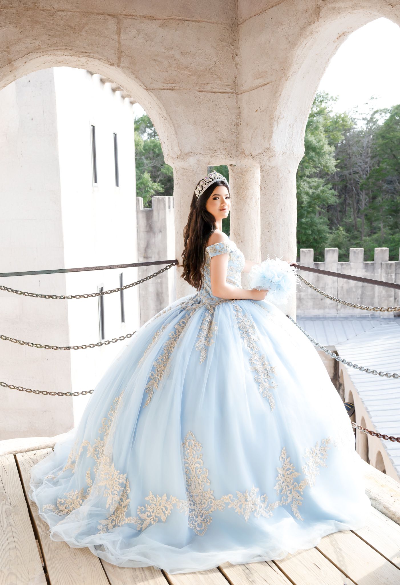 Woman in a light blue ballgown with lace details poses in an ornate white archway.