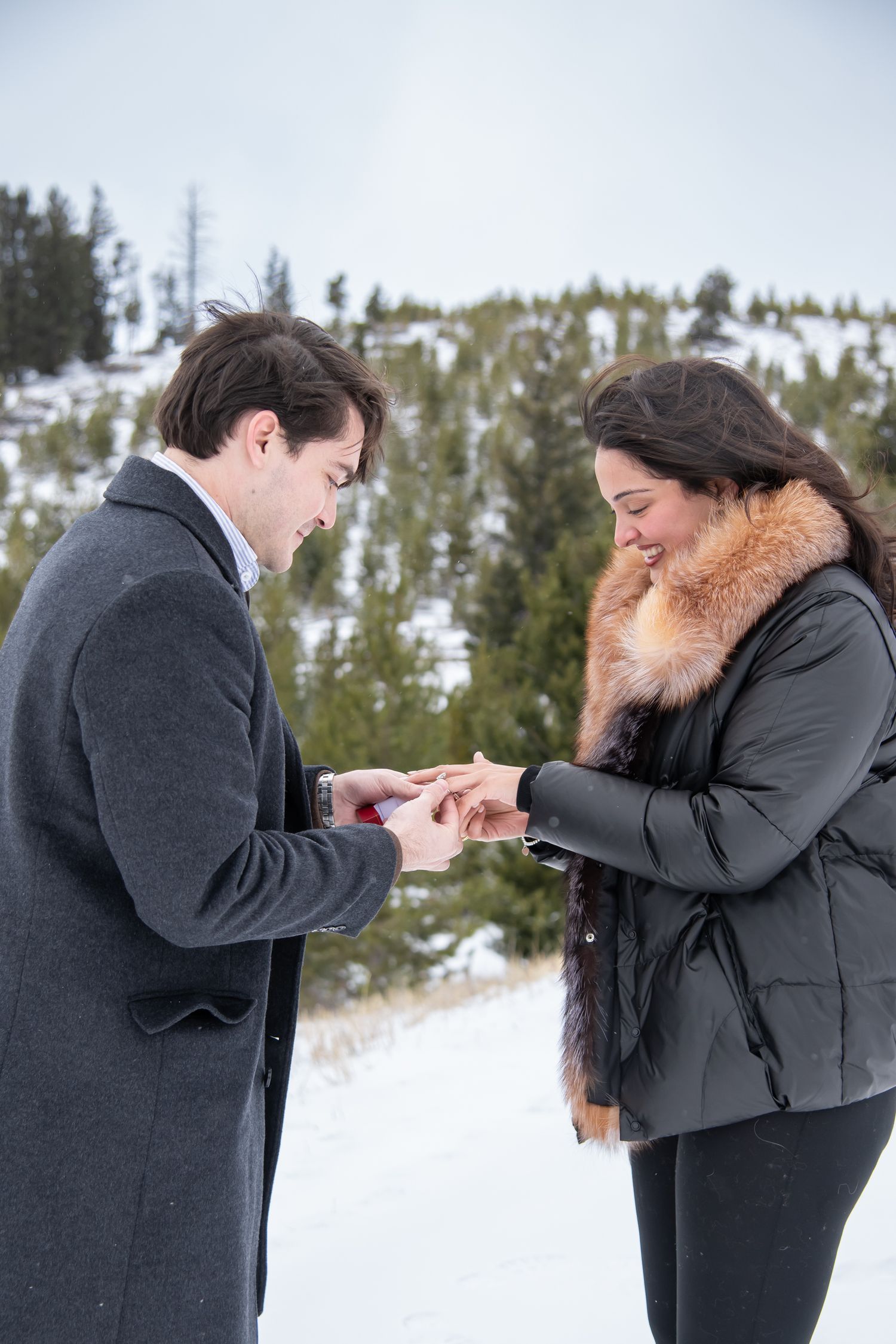A romantic winter proposal moment putting on her new engagement ring with snow and trees in the back at Sapphire Point Colorado.