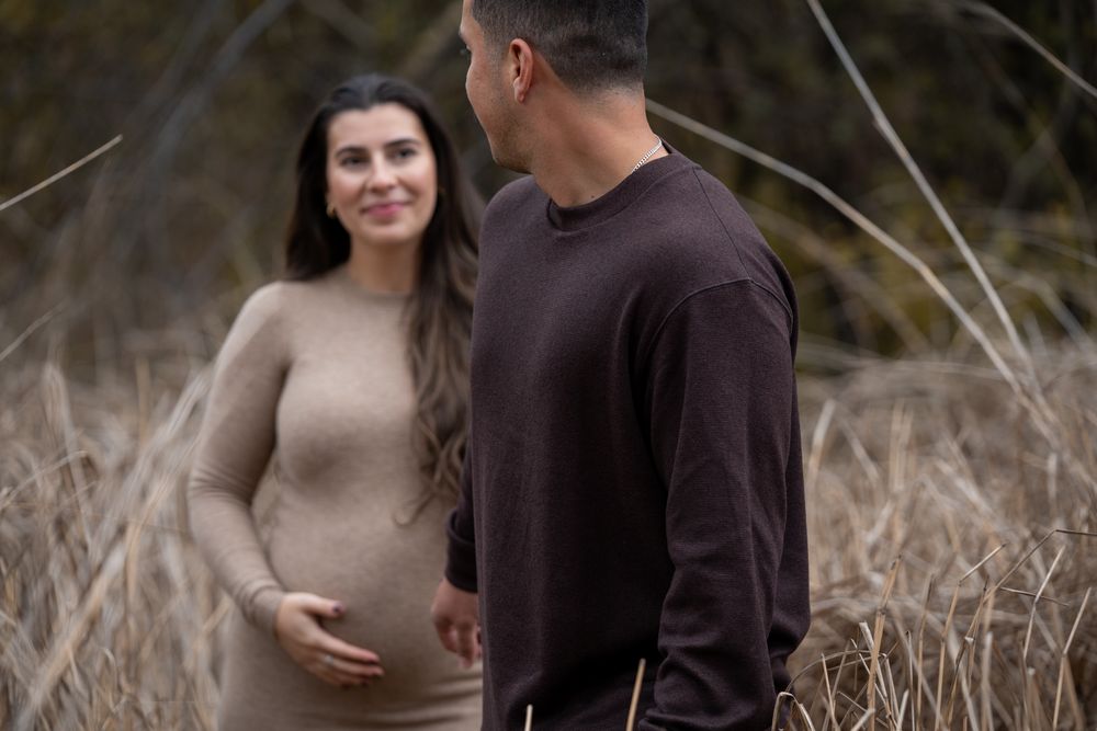 Romantic couple in casual attire embraces in a field of tall dried grass during an outdoor photo session.