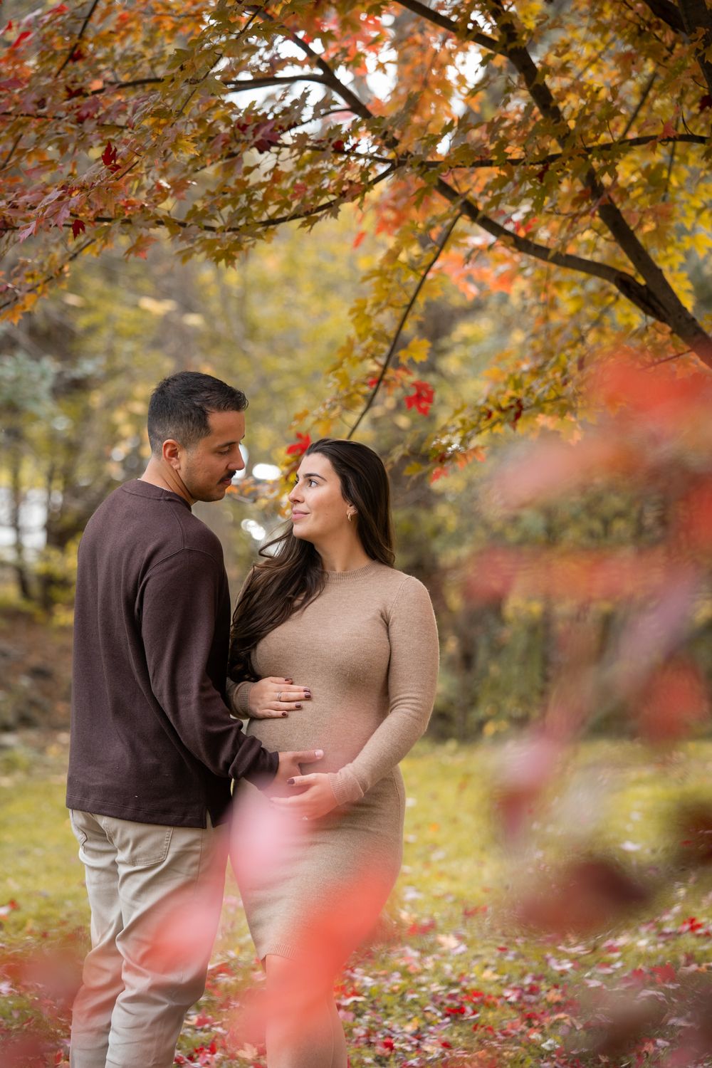 A romantic autumn scene with a couple embracing under golden maple trees with red leaves falling in the background.