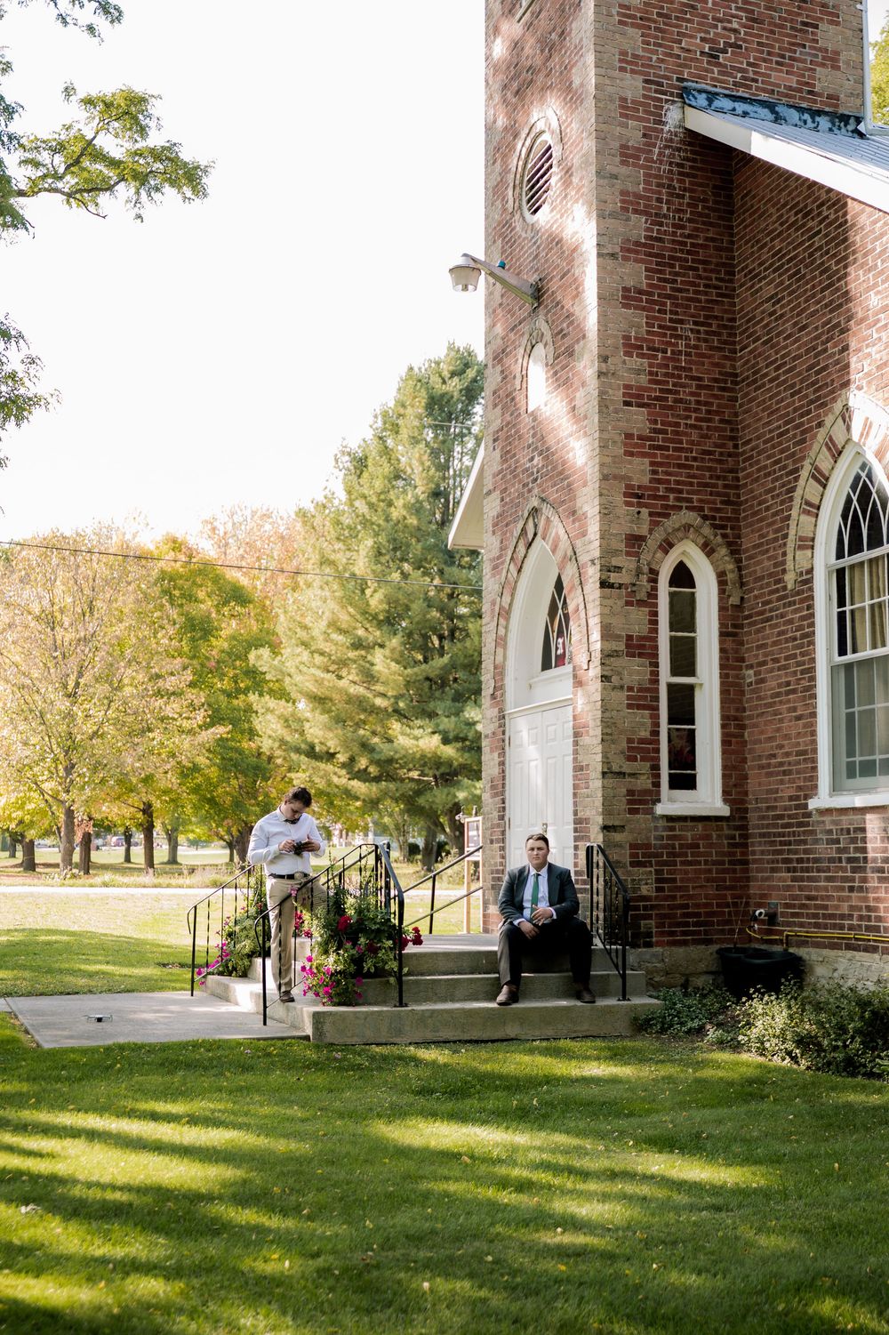 Exterior view of a traditional red brick church building with arched windows and green lawn on a sunny day.