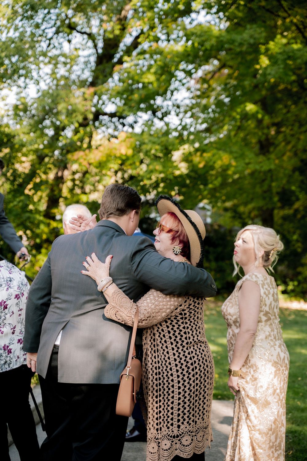 A sequence of four candid moments showing emotional embraces between loved ones at an outdoor gathering in a park setting.