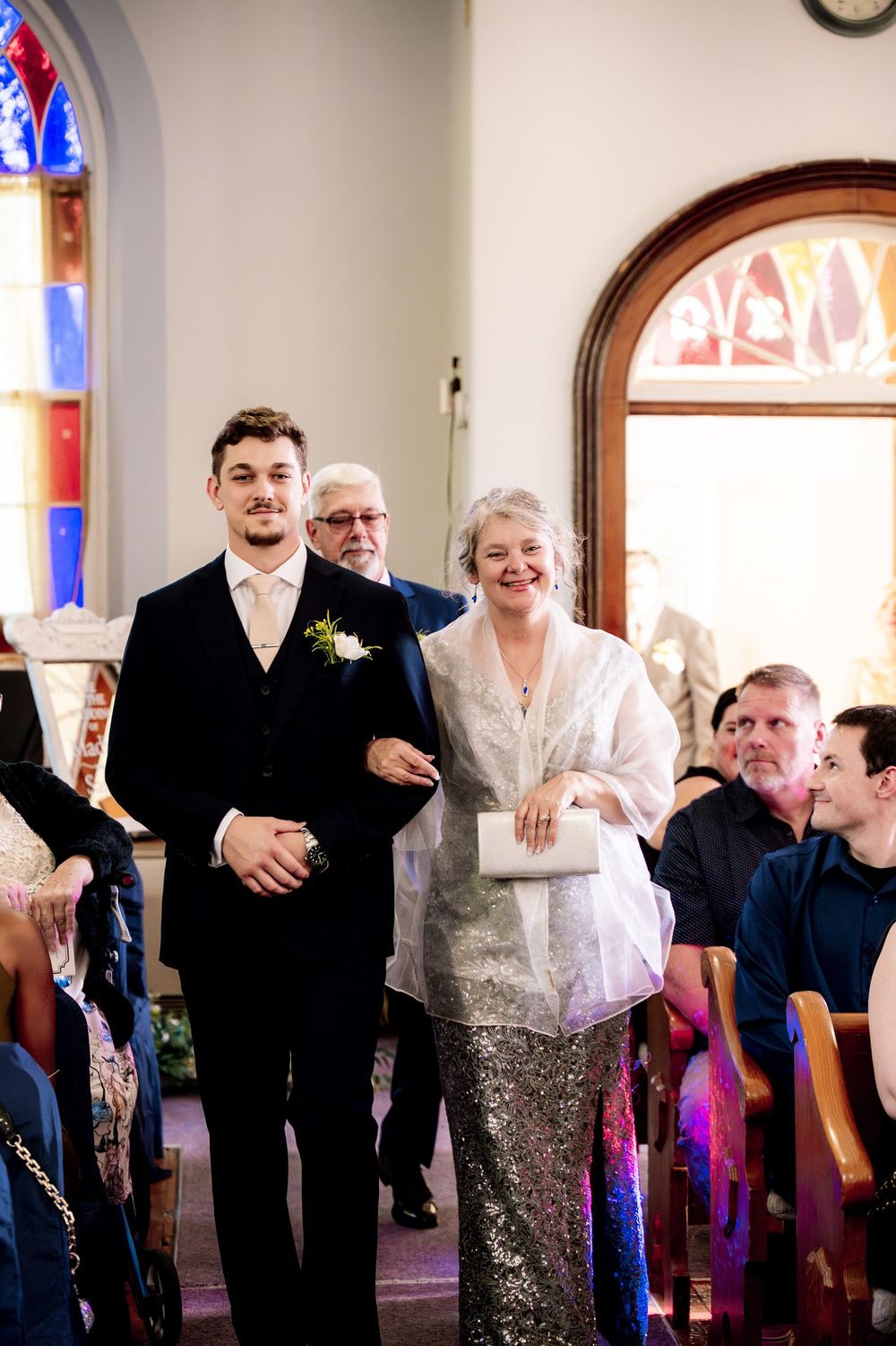 Wedding ceremony in a church with stained glass windows and arched doorways as attendees gather in the pews.