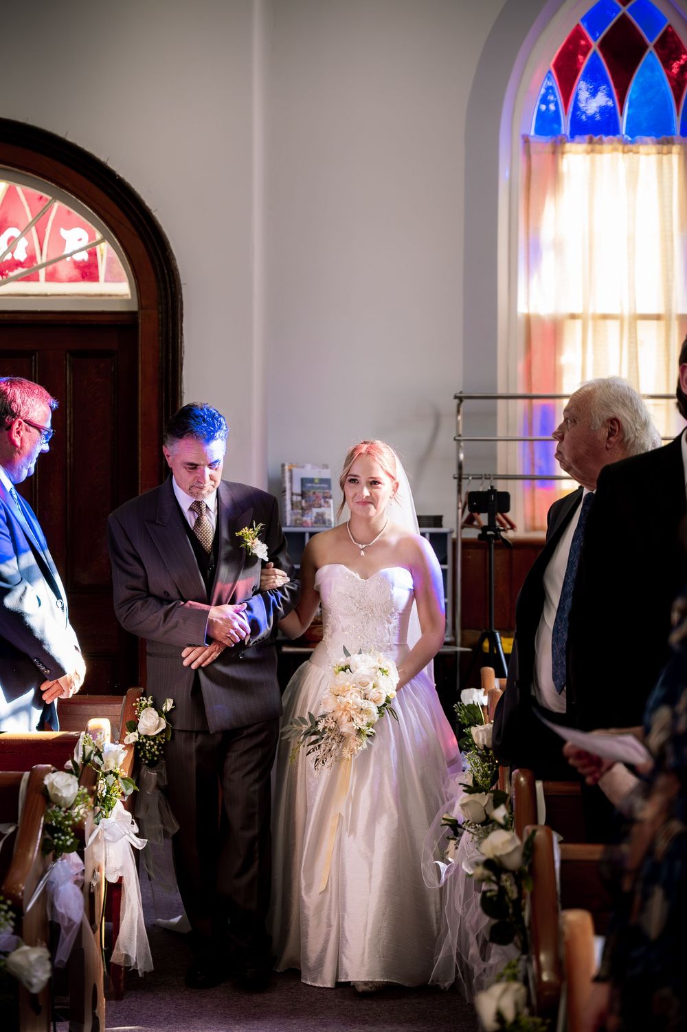 Traditional church wedding ceremony with stained glass windows and floral decorations along the aisle.
