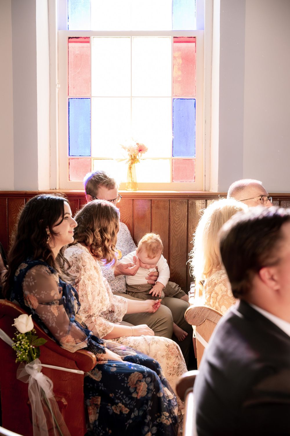 Wedding guests sit in church pews during a ceremony with natural light streaming through windows.