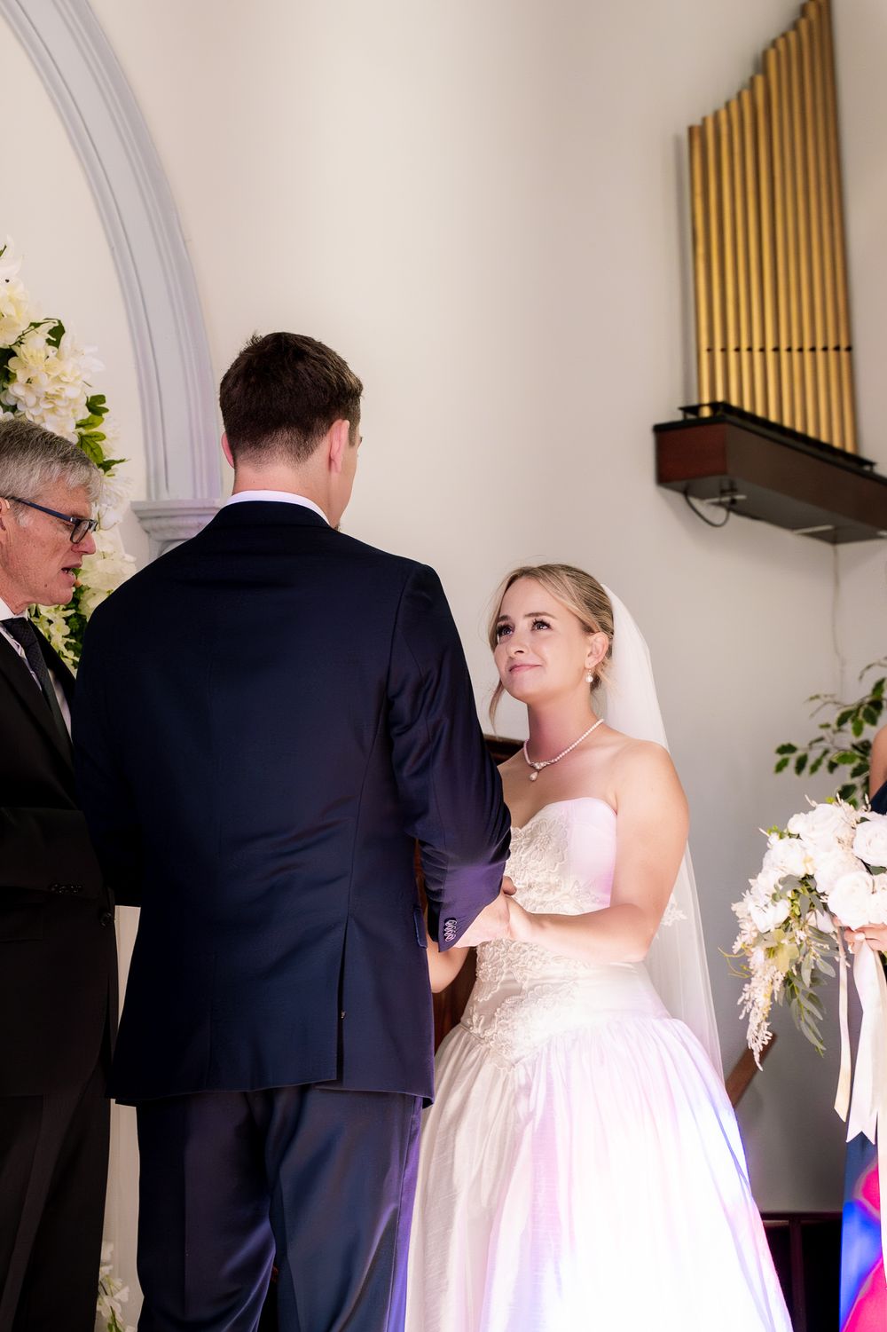 Wedding ceremony in progress inside historic church with organ pipes visible on wall.
