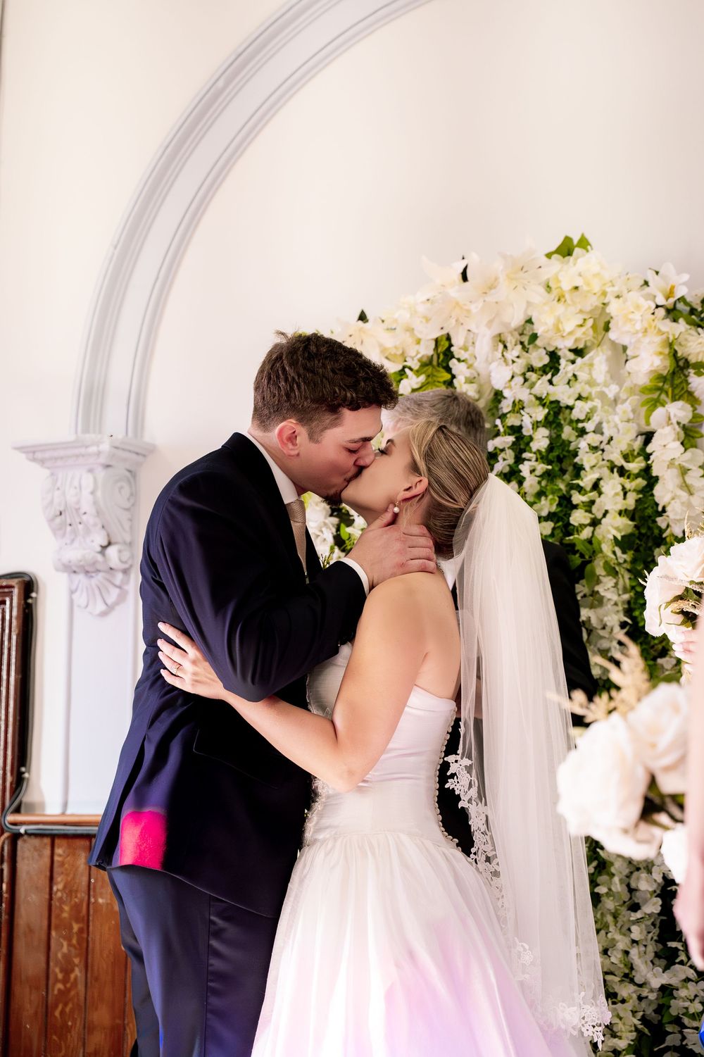 Elegant white floral arch decorates a church altar during an intimate wedding ceremony.