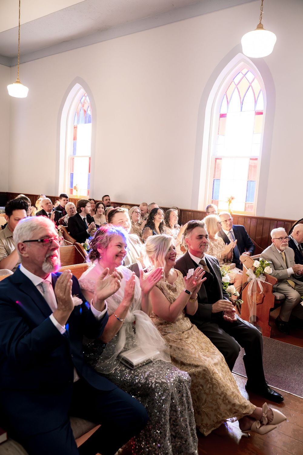 Wedding guests blow bubbles in celebration inside a church with arched windows during a joyous ceremony.