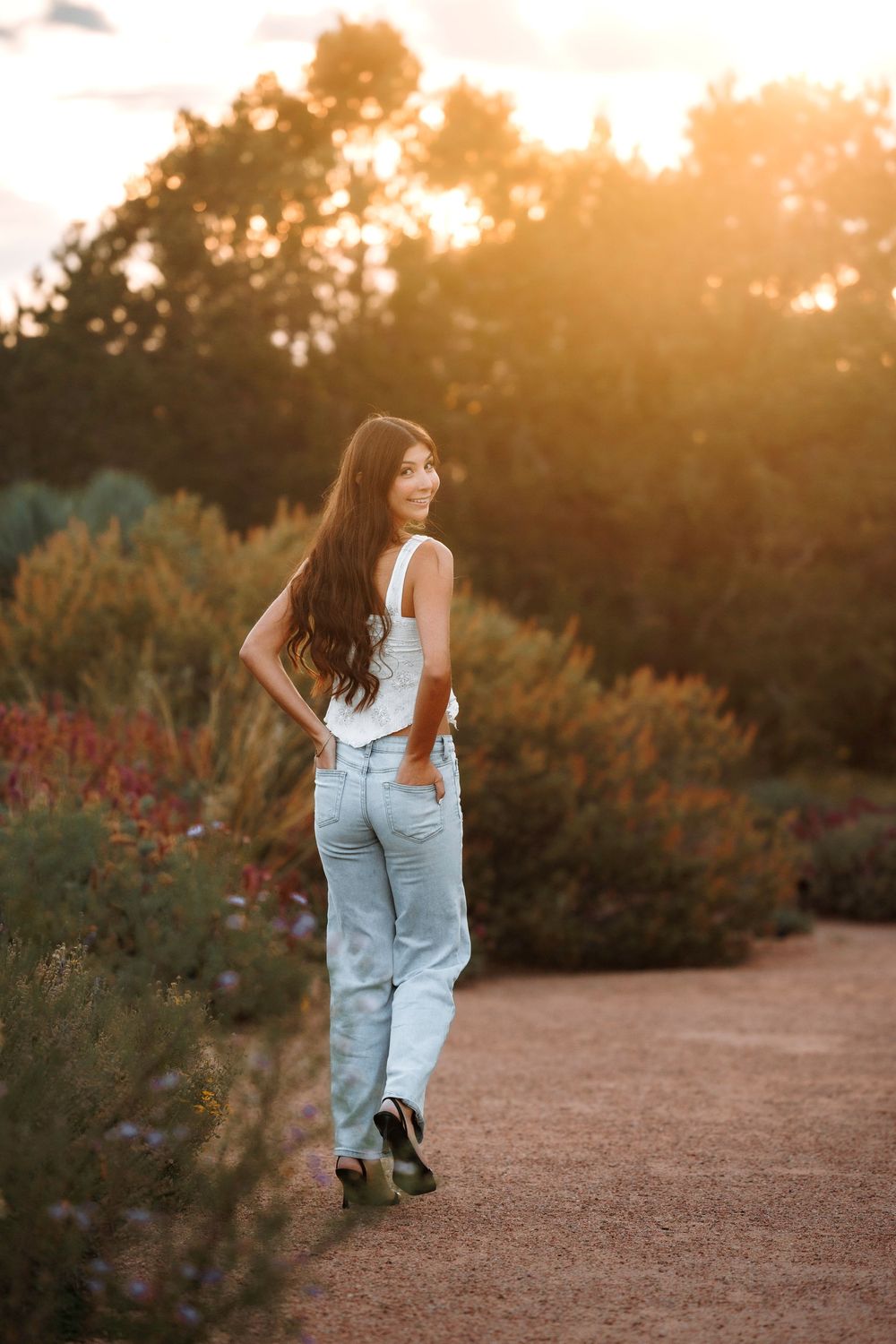 Santa Fe senior in white top and jeans walking on garden path bathed in warm golden sunset light.