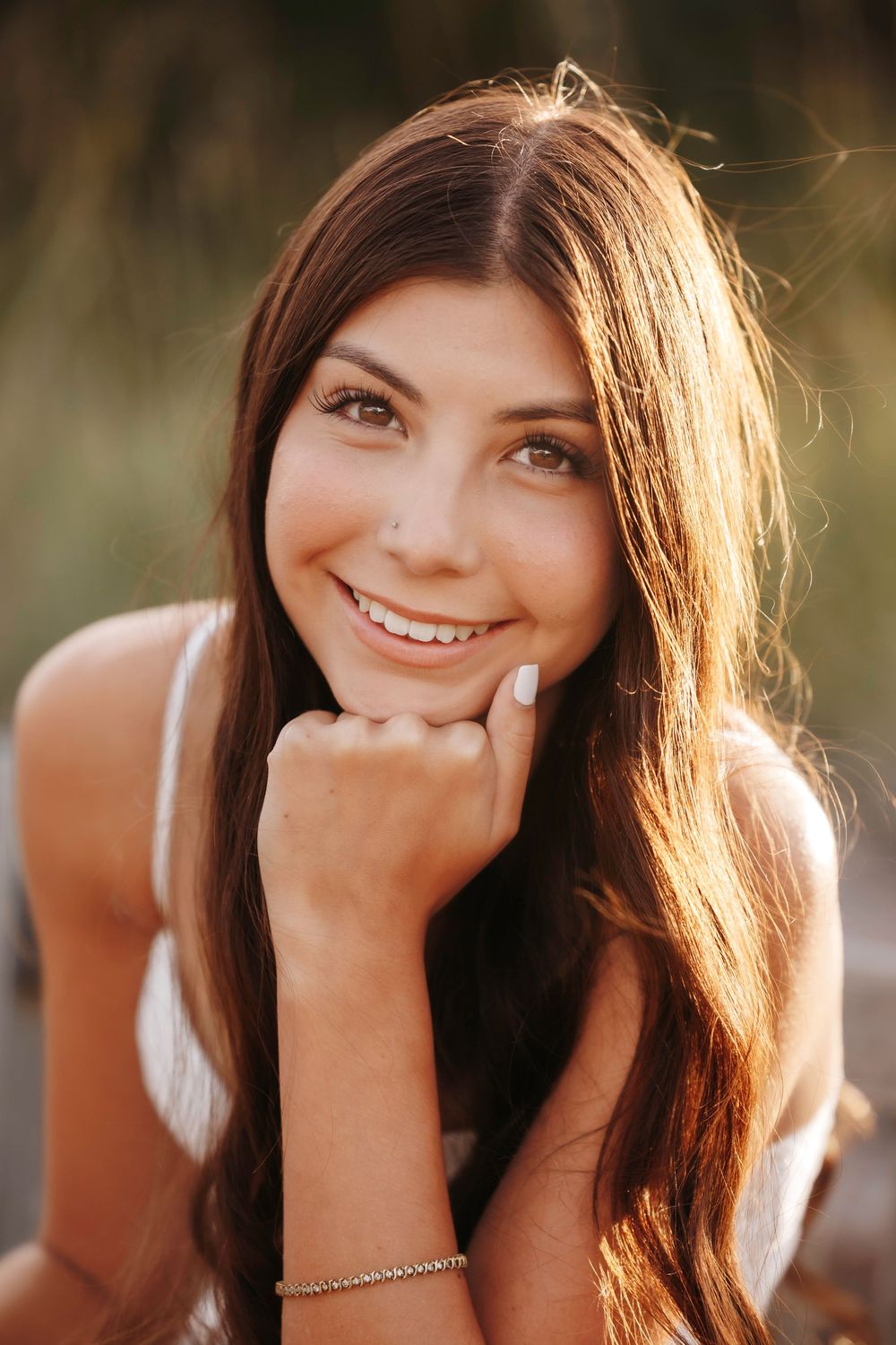 Close-up portrait of a smiling teenage girl with long brown hair in warm golden sunlight.