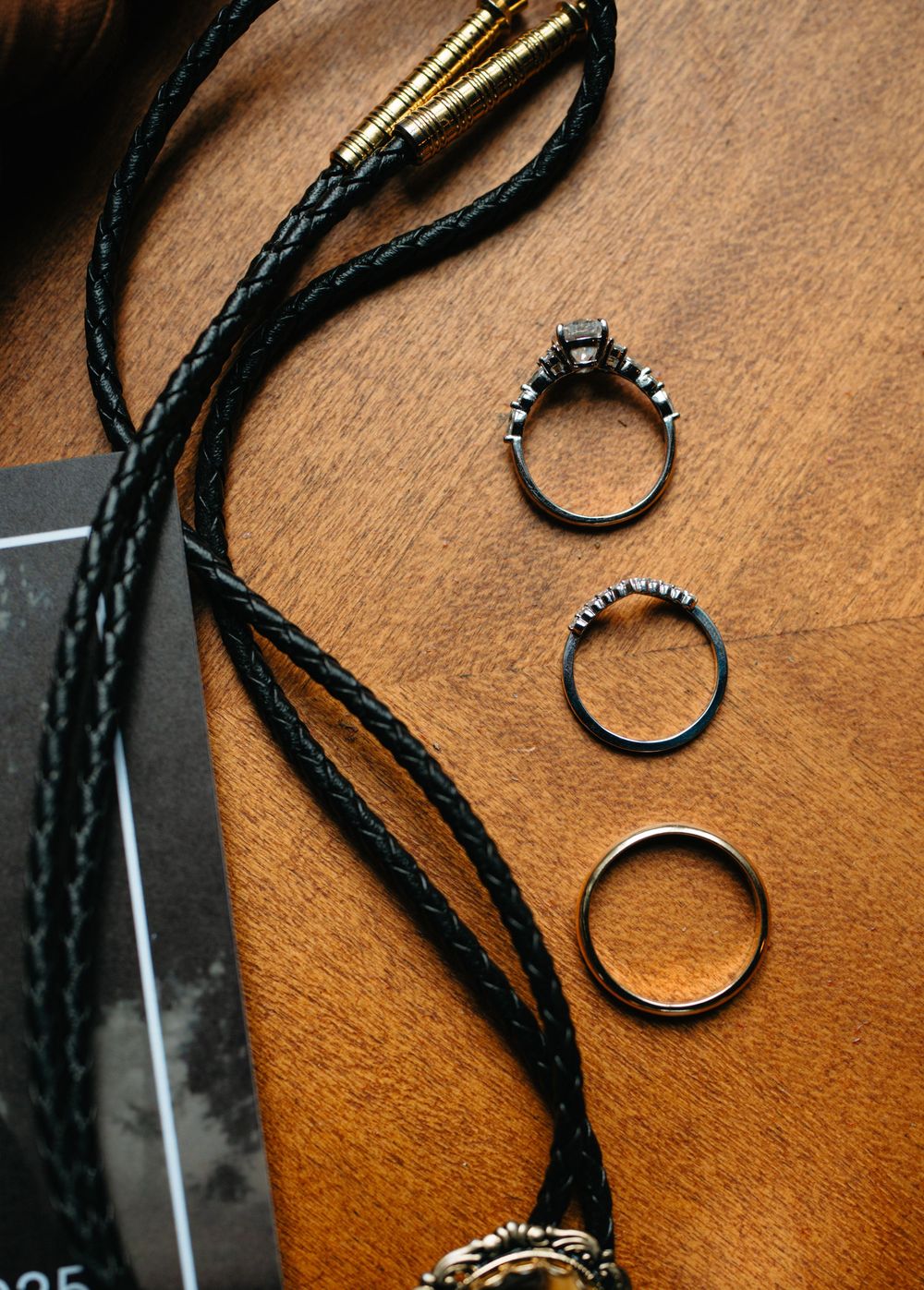Three vintage style rings and a black braided cord displayed on a wooden surface.