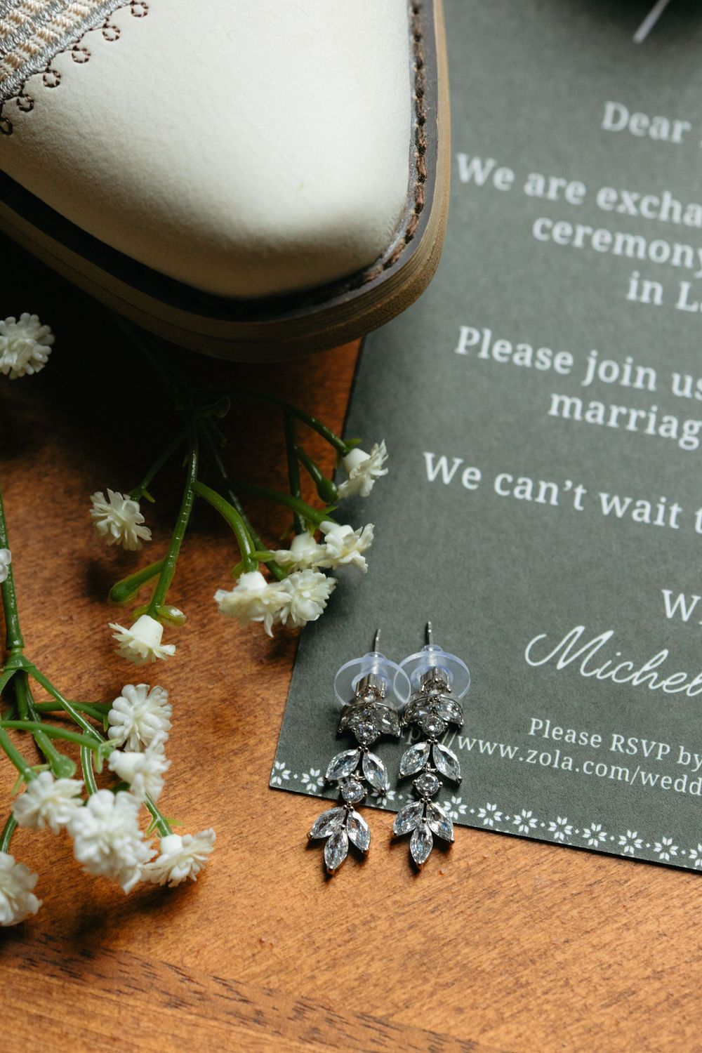 Wedding invitation details with delicate white flowers and silver butterfly earrings on a wooden surface.