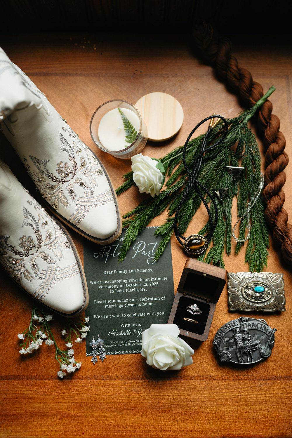 Wedding details including white shoes, evergreen sprigs, and invitation cards arranged on wooden surface.