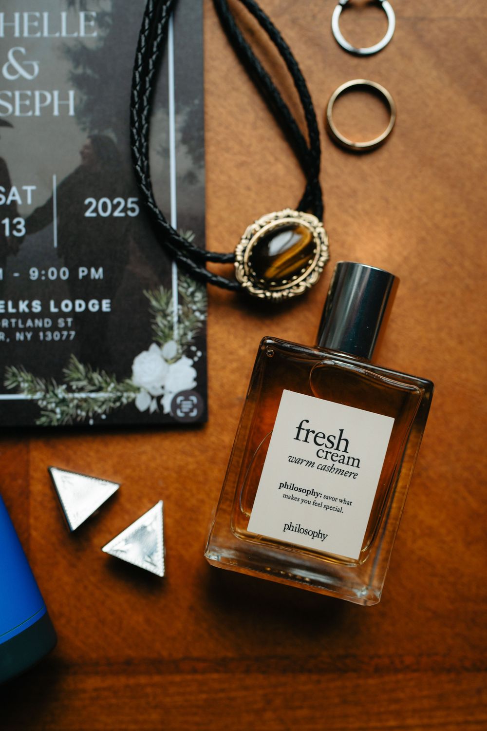 Wedding invitation, perfume bottle, jewelry and decorative elements arranged on a brown wooden surface.