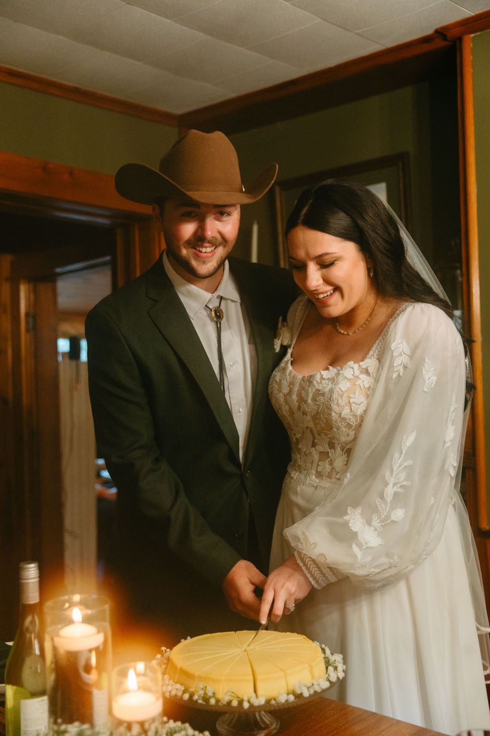 Romantic candlelit moment between newlyweds sharing smiles in warm indoor lighting.