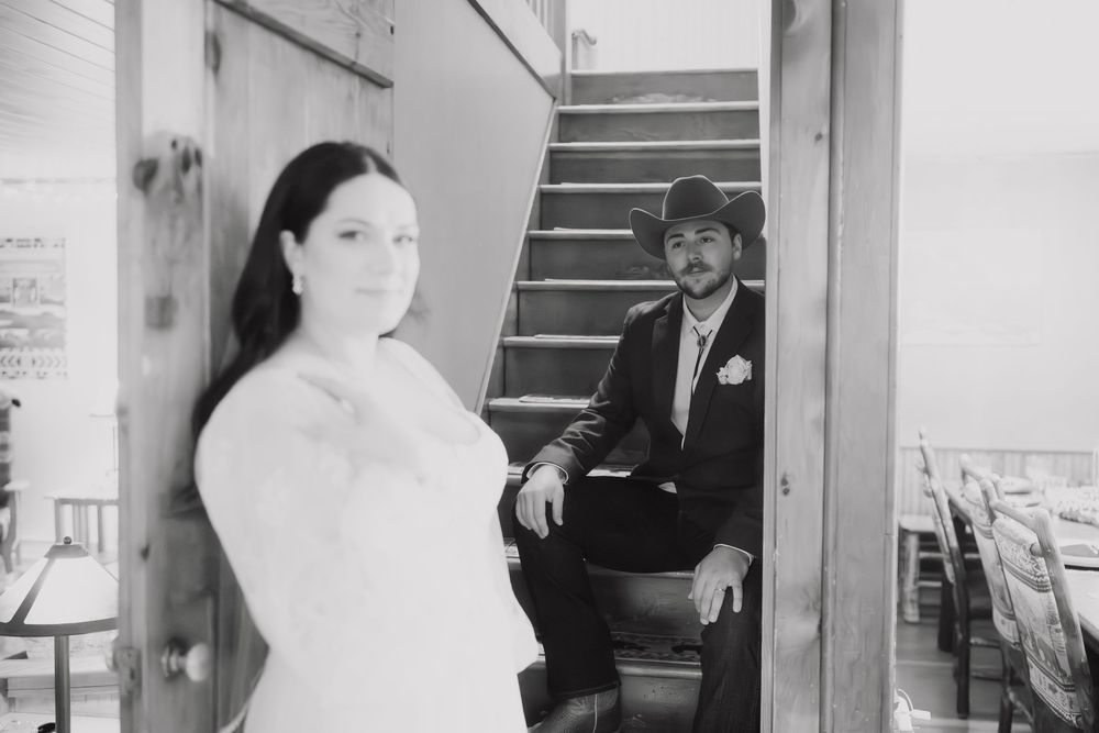 A black and white photograph shows a couple in wedding attire posing in a stairwell.