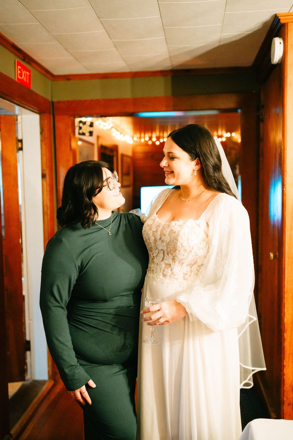 Two people share an intimate moment in a warmly lit hallway, one wearing black and one in white.