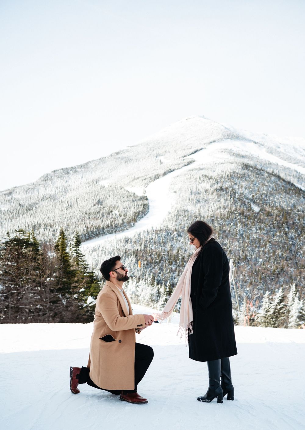 A winter proposal scene unfolds against snowy mountains as two people share a special moment in the snow.