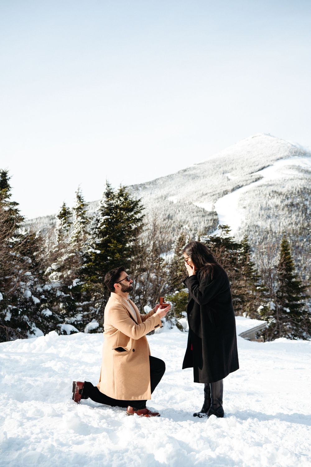 A couple shares a romantic moment in the snowy mountains during a winter proposal photoshoot.