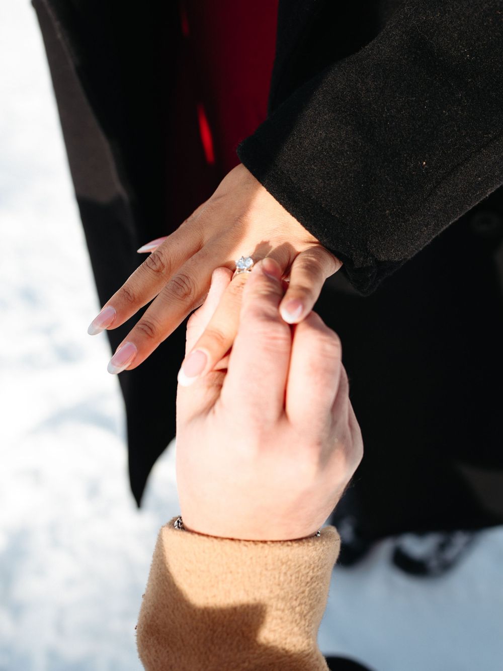 A close-up shot of hands showing an engagement ring with a sparkling diamond in natural light.