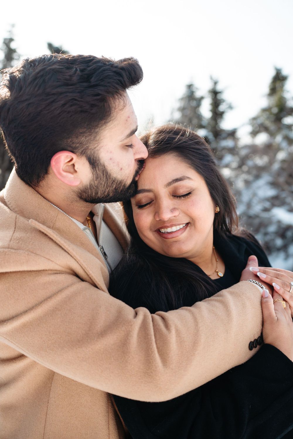 A tender moment between a couple sharing an intimate embrace against a snowy forest backdrop.