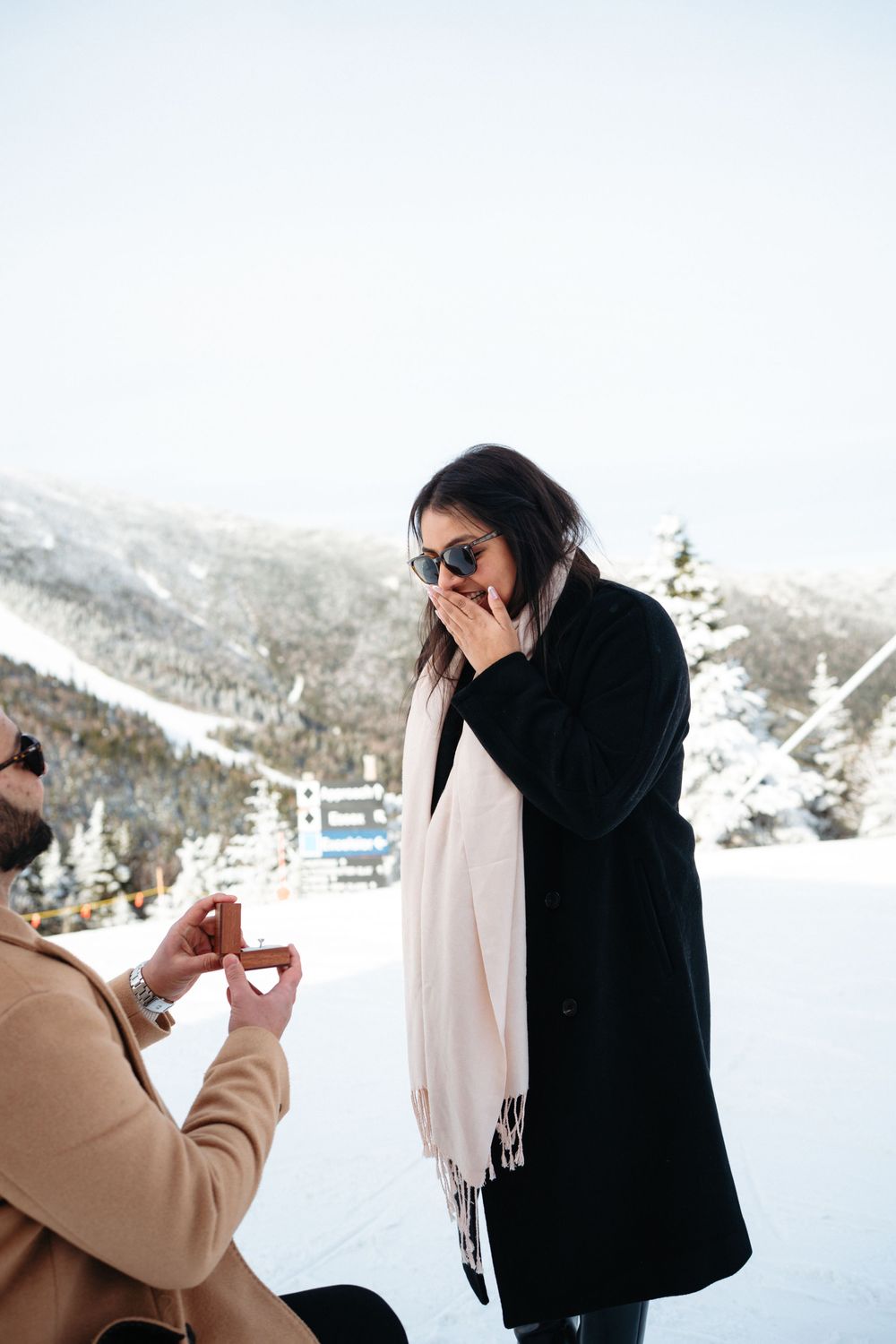 A surprise proposal moment captured at a snowy mountain ski resort with snow-covered slopes in the background.