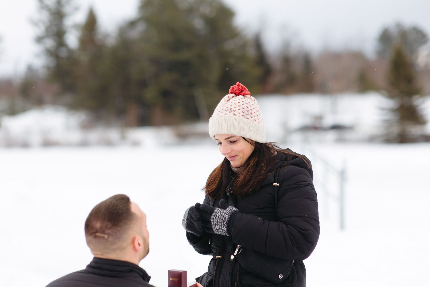 A group plays together in a snowy winter landscape with trees visible in the background.