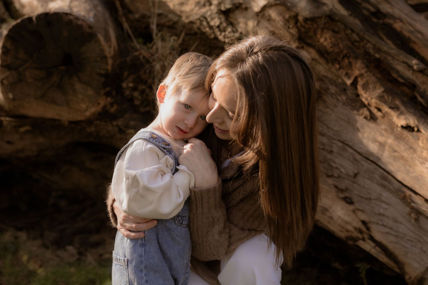 A tender moment captured between parent and child under a rustic wooden overhang in warm natural lighting.