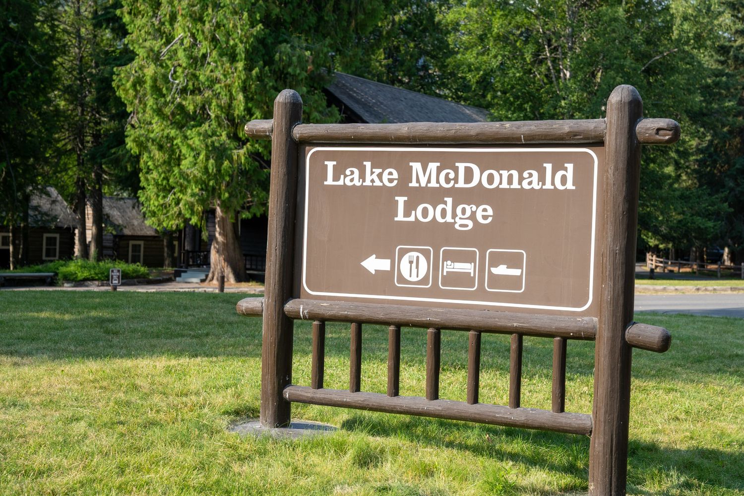 A brown wooden park sign and directional markers along a tree-lined path at Lake McDonald.