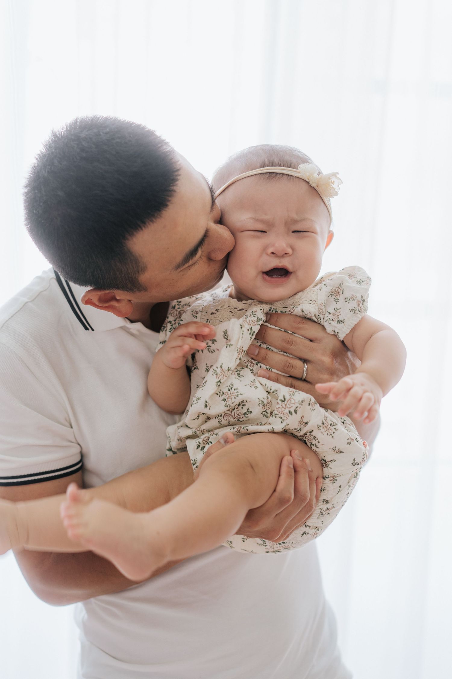 A tender moment between parent and child in soft white tones as they share cuddles and laughter on a couch.在柔和的白色調中，父母和孩子在沙發上擁抱、歡笑，溫馨的一刻。