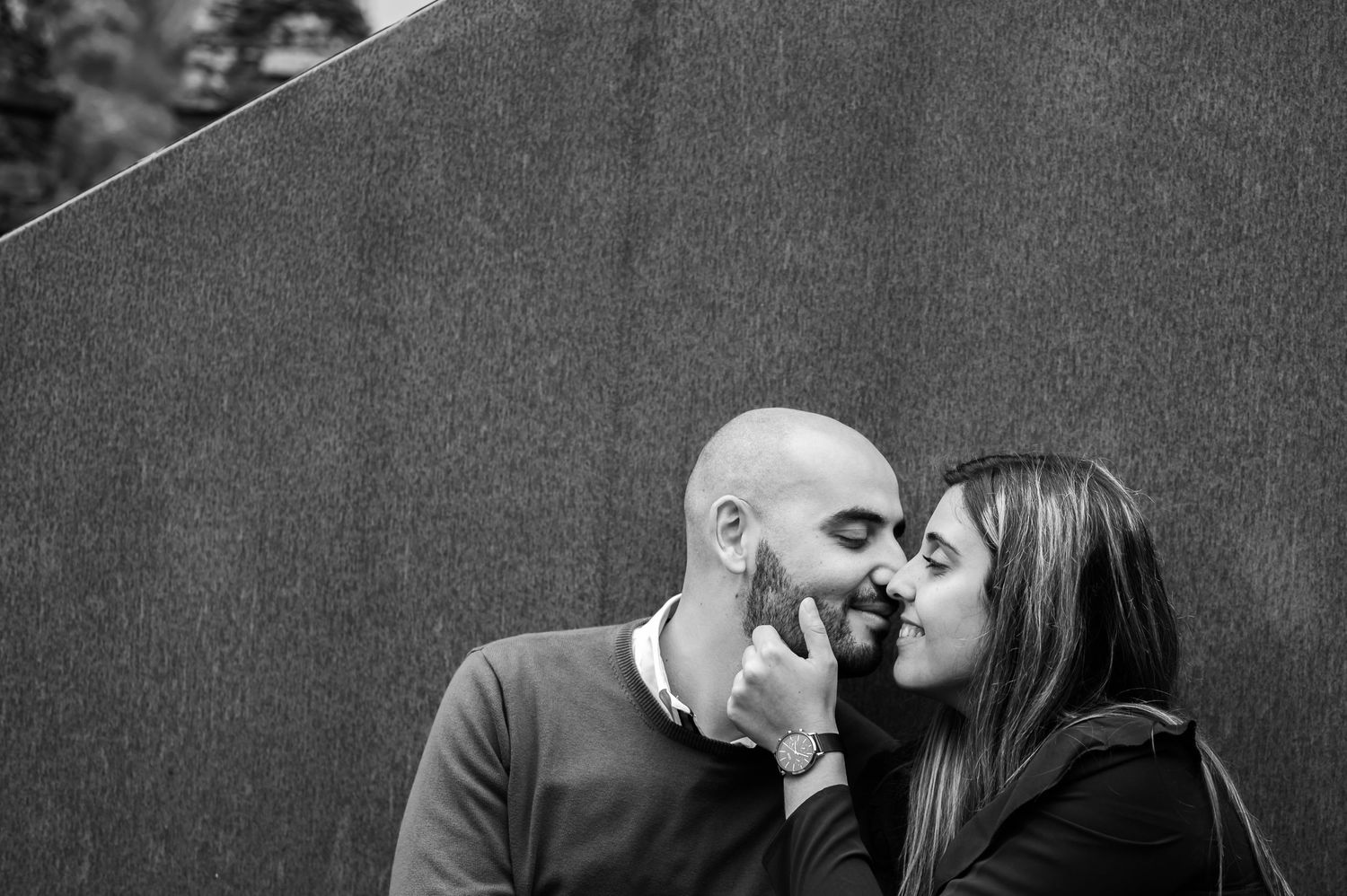 Black and white portrait of couple sharing intimate moment against dark wall.
