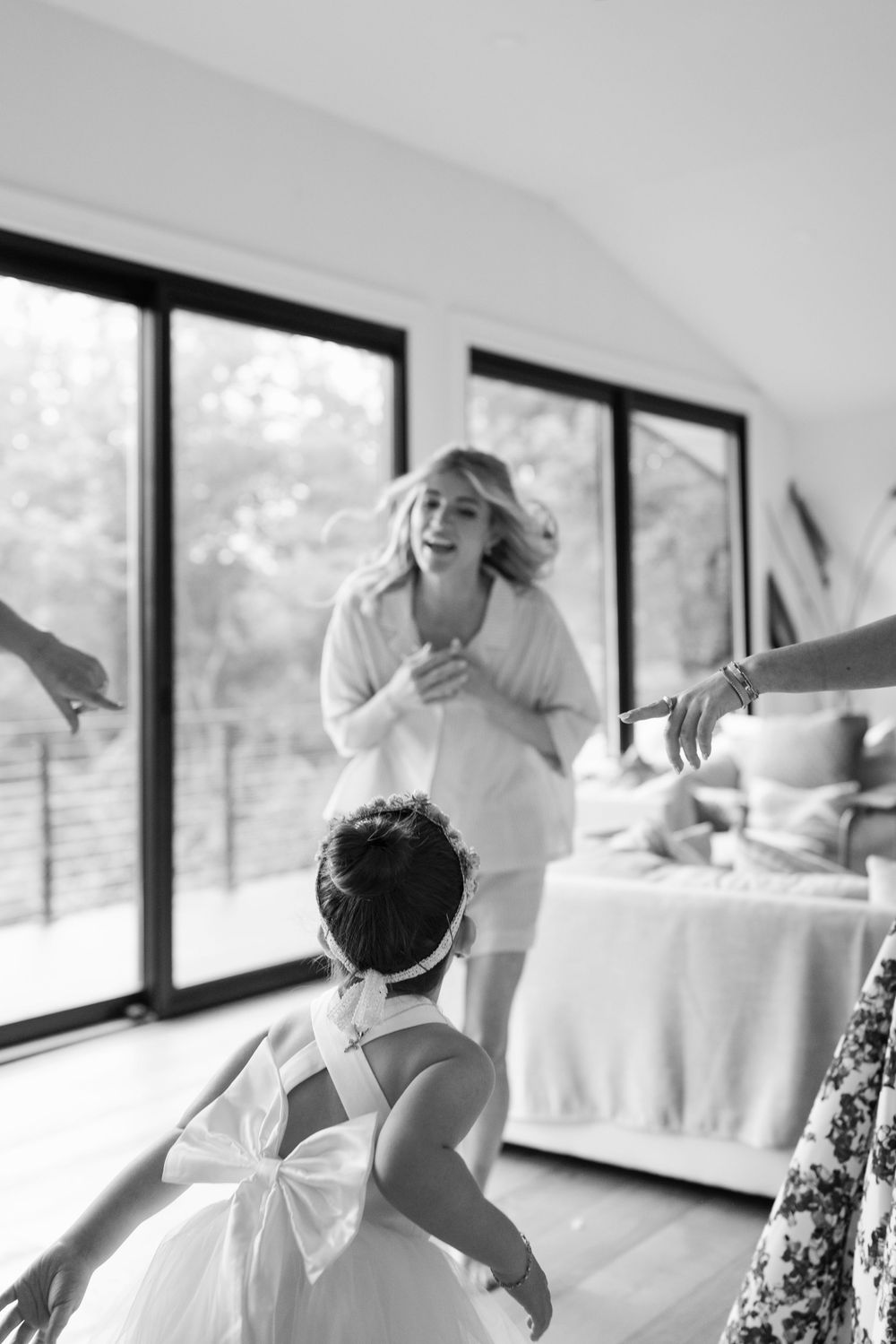 A candid black and white photo of a wedding preparation moment with a flower girl in a dress with a bow.