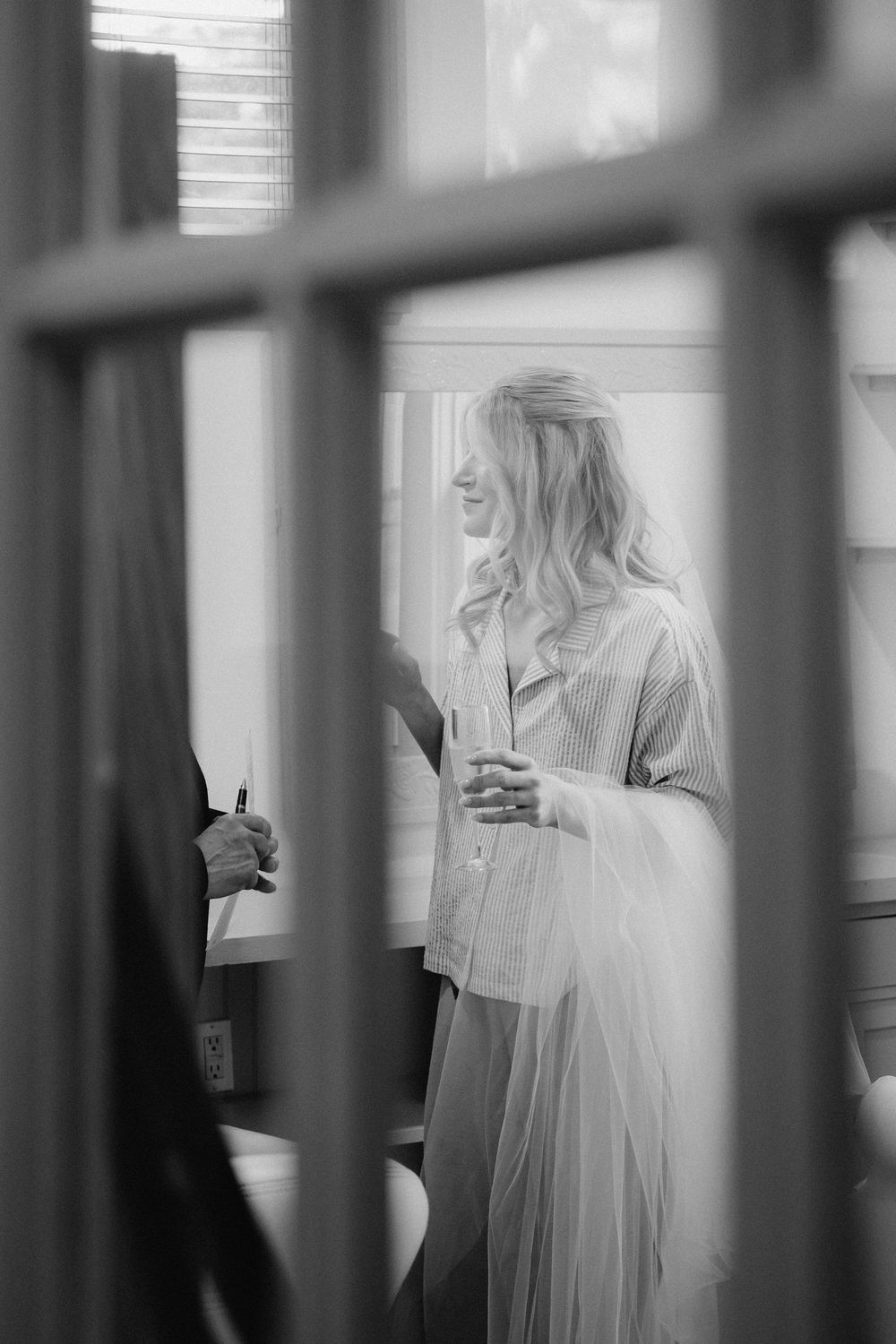 A dreamy black and white photo of a person in white clothing seen through vertical window bars or blinds.