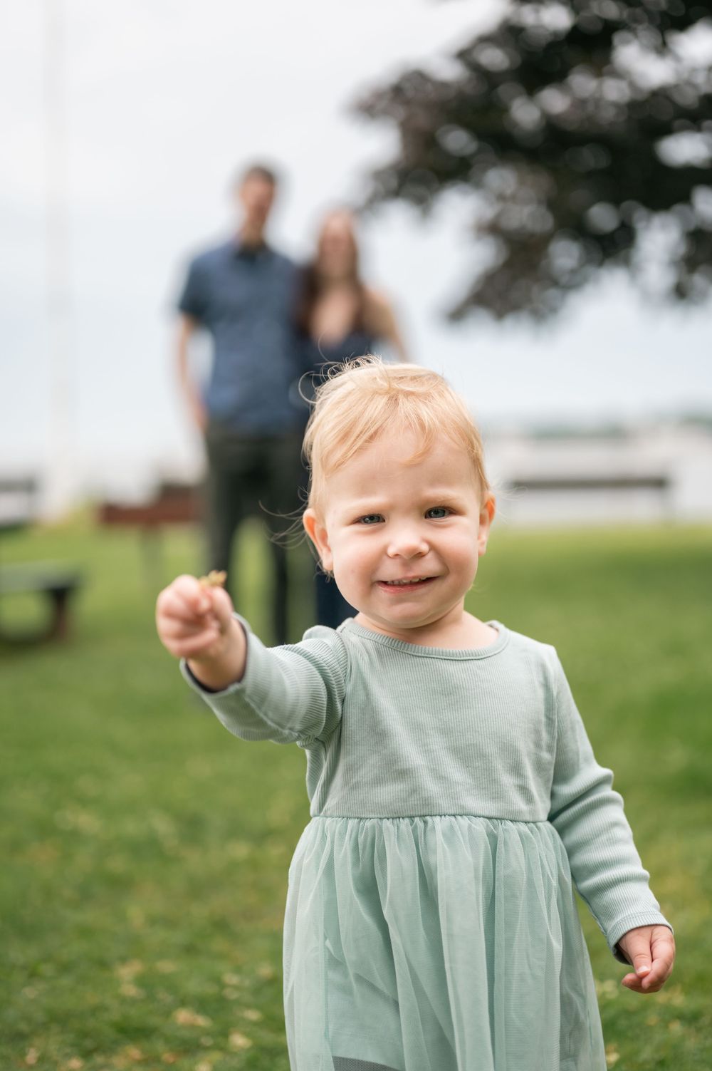 Small child in mint green dress playing on grassy hill during outdoor photoshoot. Mini Session Branford point branford Connecticut