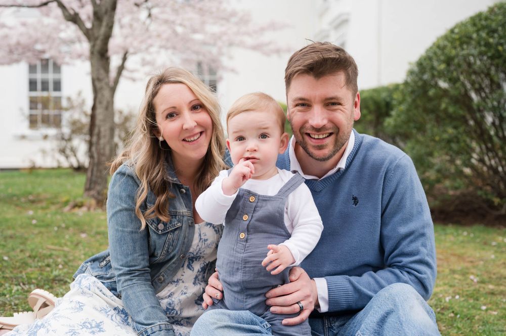 A family shares joyful moments together on a lawn with cherry blossoms in the background. Cherry Blossom Mini Sessions Branford CT