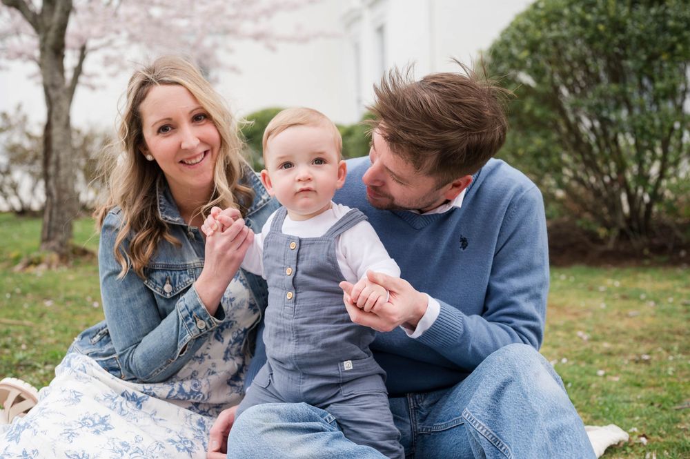 A happy family plays together on grass under blooming spring trees. Cherry Blossom Mini Sessions Branford CT