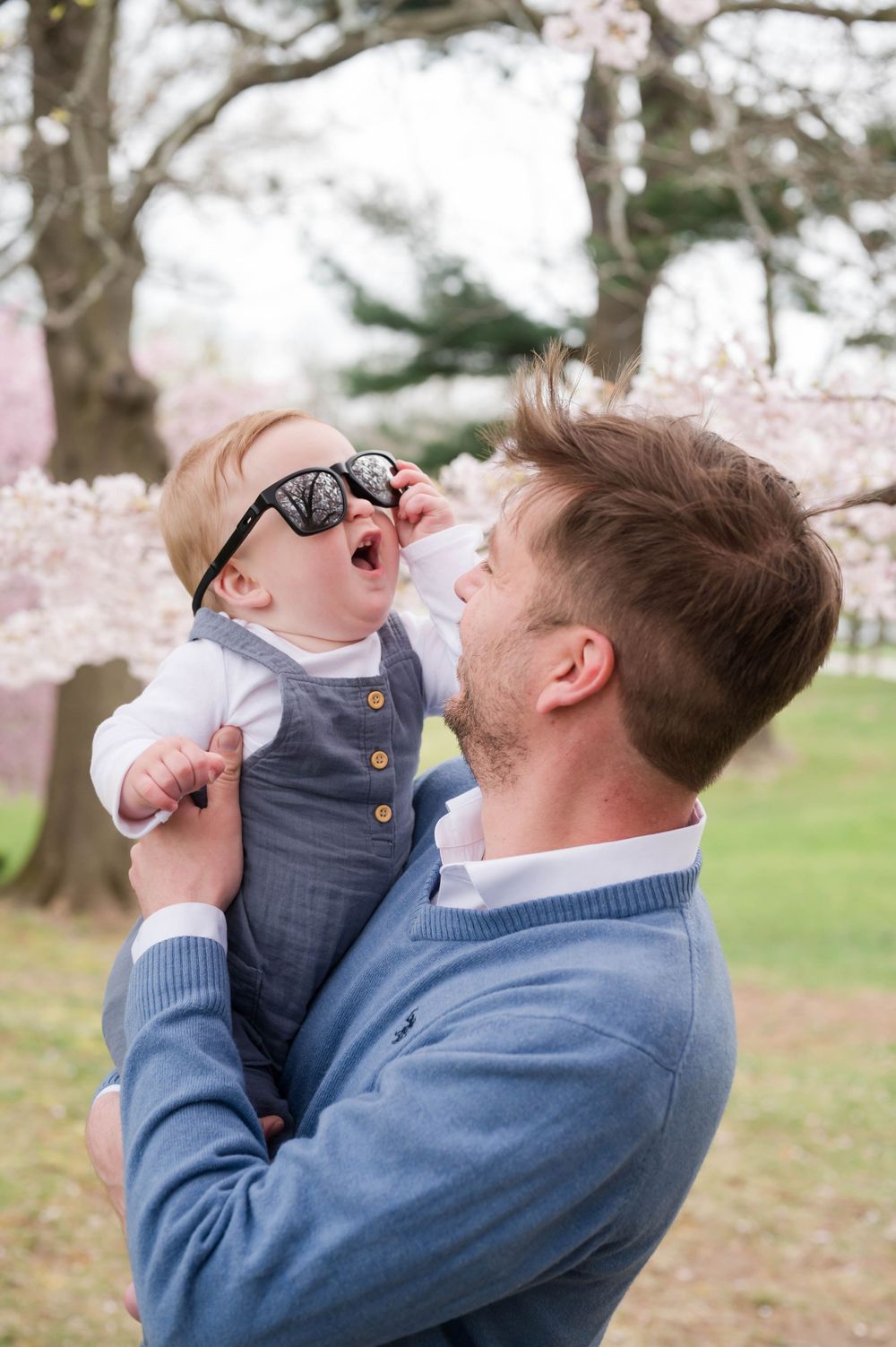 A joyful parent and baby share a playful moment under blooming cherry trees. Cherry Blossom Mini Sessions Branford CT