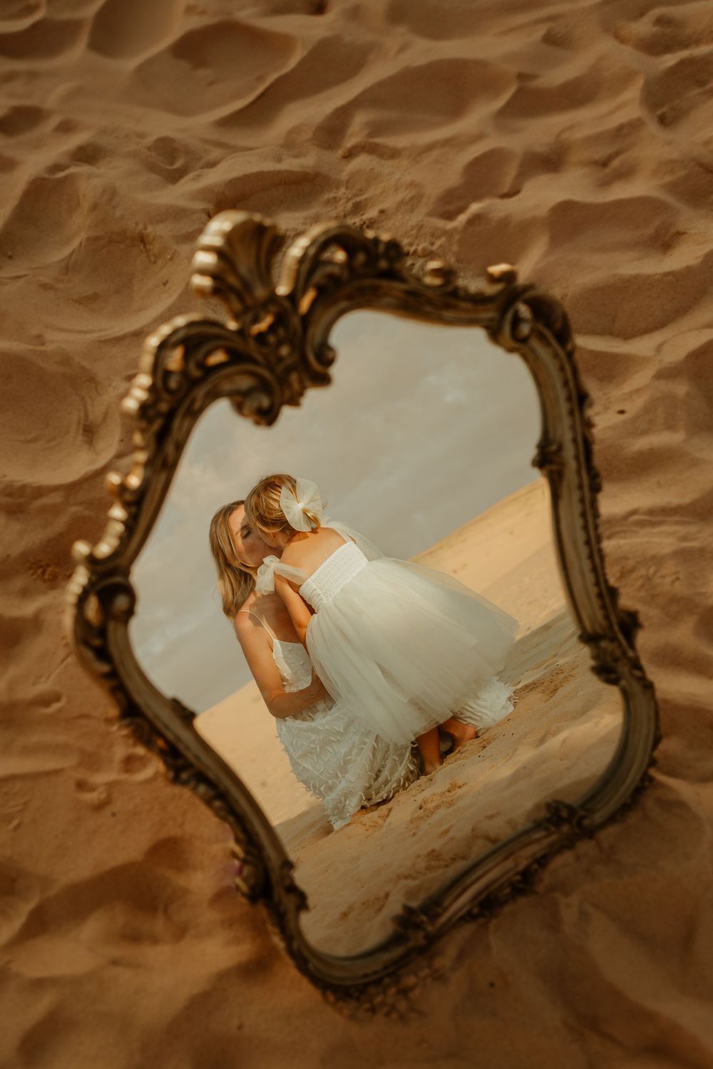An ornate vintage mirror placed in sand reflects Kurnell beach scene with a Motherhood photoshoot by Sydney photographer.