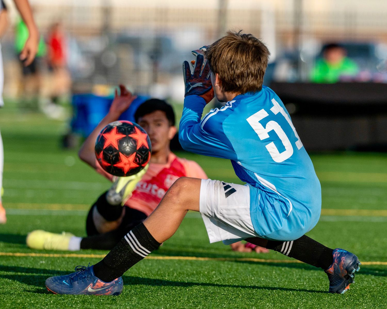 Youth soccer goalkeeper preparing to make save as striker attempts shot.