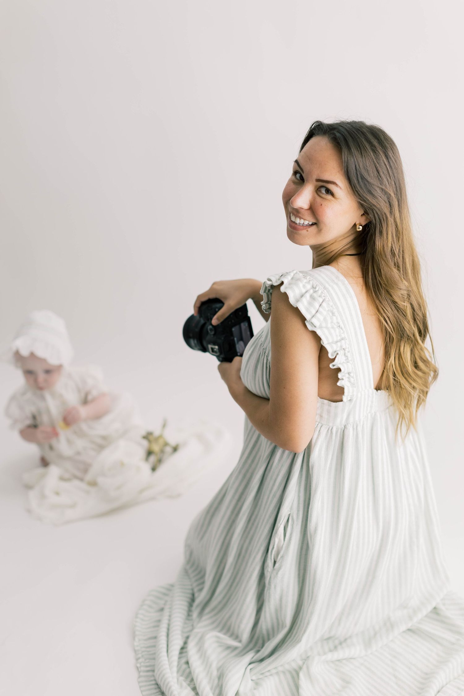 A photographer in a flowing white dress twirls playfully while holding a camera in a bright studio setting.