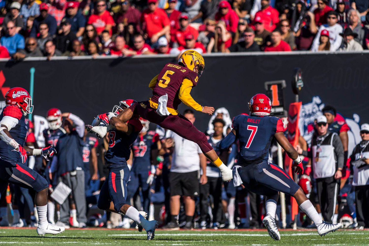 Football player in gold uniform leaps high over opponents during game action.