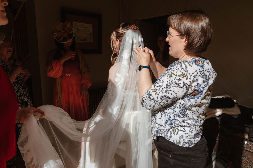 Elmore Court Wedding by Cotswolds Zara Davis Photography in Gloucestershire putting the brides veil on